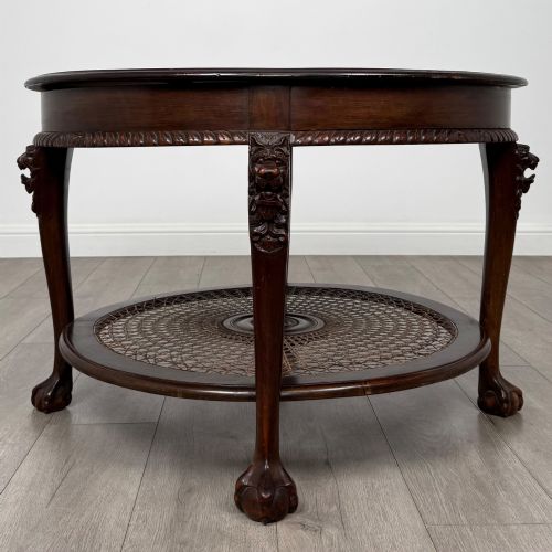fig 3. A circular dark mahogany coffee table featuring carved lion heads atop cabriole legs ending in claw and ball feet, with a woven cane lower shelf.