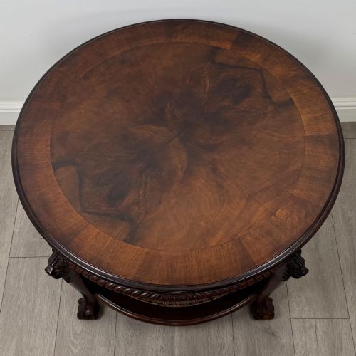 fig 4. A circular dark mahogany coffee table featuring carved lion heads atop cabriole legs ending in claw and ball feet, with a woven cane lower shelf.
