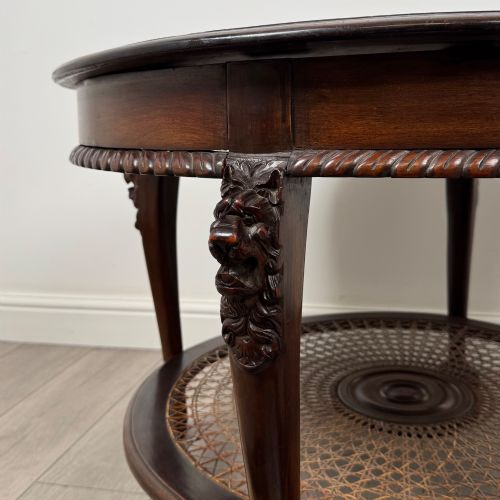 fig 5. A circular dark mahogany coffee table featuring carved lion heads atop cabriole legs ending in claw and ball feet, with a woven cane lower shelf.