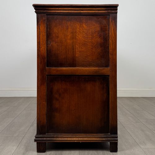 fig 3. A twentieth-century warm oak sideboard featuring three upper drawers with brass handles above three cupboard doors decorated with geometric moulded panels and exterior brass H-hinges.