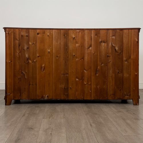 fig 5. A twentieth-century warm oak sideboard featuring three upper drawers with brass handles above three cupboard doors decorated with geometric moulded panels and exterior brass H-hinges.