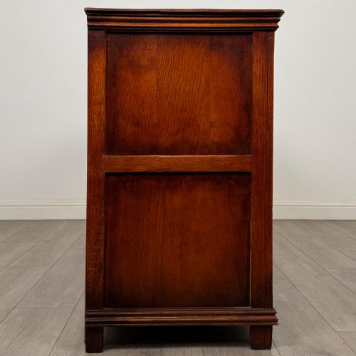 fig 7. A twentieth-century warm oak sideboard featuring three upper drawers with brass handles above three cupboard doors decorated with geometric moulded panels and exterior brass H-hinges.