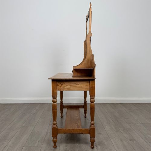 fig 2. A Victorian pitch pine dressing table featuring a central swivel mirror, side scroll shelves, frieze drawers with brass handles, and turned legs with a low shelf.