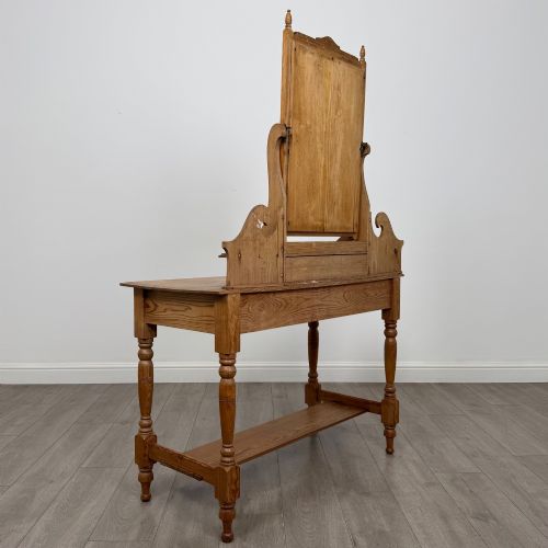 fig 3. A Victorian pitch pine dressing table featuring a central swivel mirror, side scroll shelves, frieze drawers with brass handles, and turned legs with a low shelf.
