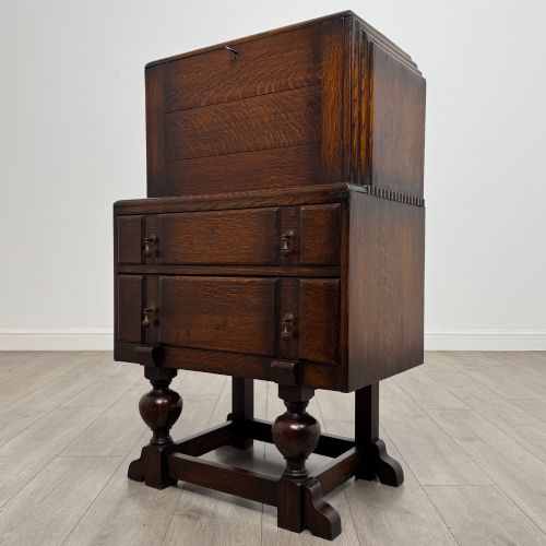 fig 2. An early 20th-century dark oak writing bureau featuring a sloped fall-front lid above two drawers, supported on turned bulbous legs with stretchers.