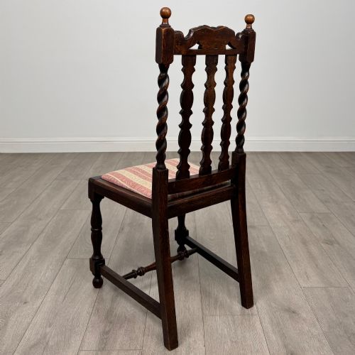 fig 2. A set of four dark oak dining chairs with barley twist side supports, carved top crests, vertically slatted backrests, and striped fabric seat cushions.