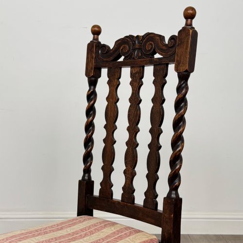 fig 3. A set of four dark oak dining chairs with barley twist side supports, carved top crests, vertically slatted backrests, and striped fabric seat cushions.