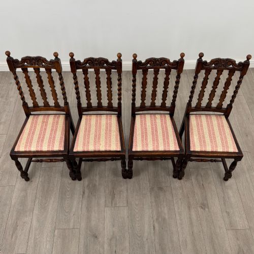 fig 6. A set of four dark oak dining chairs with barley twist side supports, carved top crests, vertically slatted backrests, and striped fabric seat cushions.