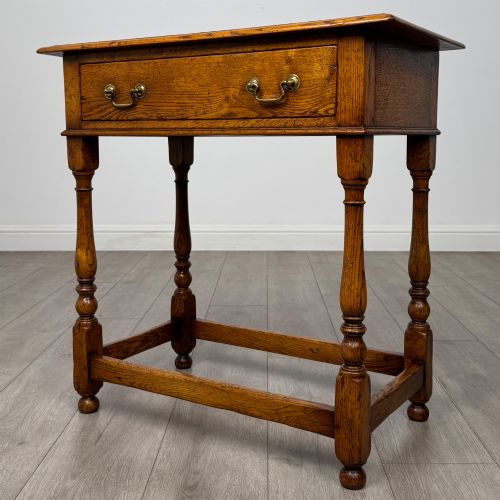 fig 1. A golden oak side table featuring a single drawer with two brass handles, turned legs, and an lower stretcher base.