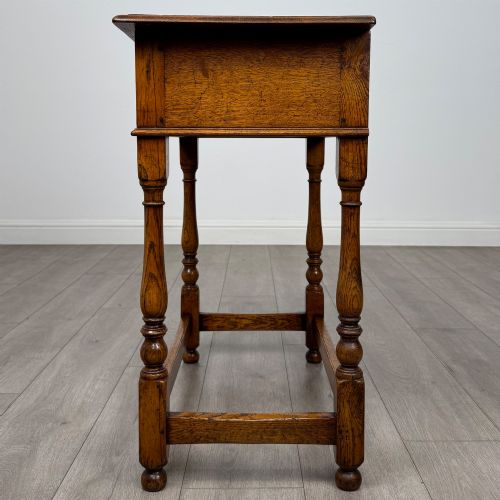 fig 2. A golden oak side table featuring a single drawer with two brass handles, turned legs, and an lower stretcher base.