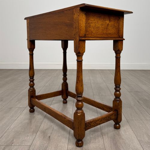 fig 5. A golden oak side table featuring a single drawer with two brass handles, turned legs, and an lower stretcher base.