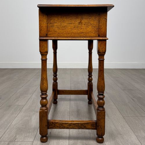 fig 6. A golden oak side table featuring a single drawer with two brass handles, turned legs, and an lower stretcher base.