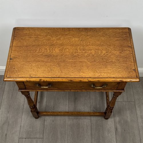 fig 8. A golden oak side table featuring a single drawer with two brass handles, turned legs, and an lower stretcher base.