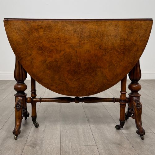 fig 1. A 19th-century Victorian Sutherland table crafted from burr walnut featuring folded drop leaves, turned twin-column supports, and carved legs on brass castors.