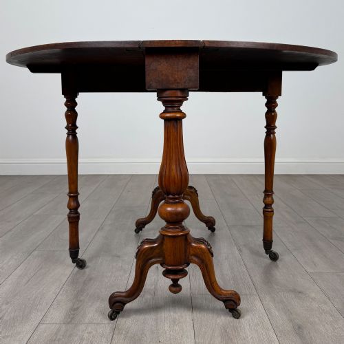 fig 4. A 19th-century Victorian Sutherland table crafted from burr walnut featuring folded drop leaves, turned twin-column supports, and carved legs on brass castors.