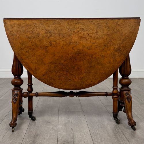 fig 6. A 19th-century Victorian Sutherland table crafted from burr walnut featuring folded drop leaves, turned twin-column supports, and carved legs on brass castors.