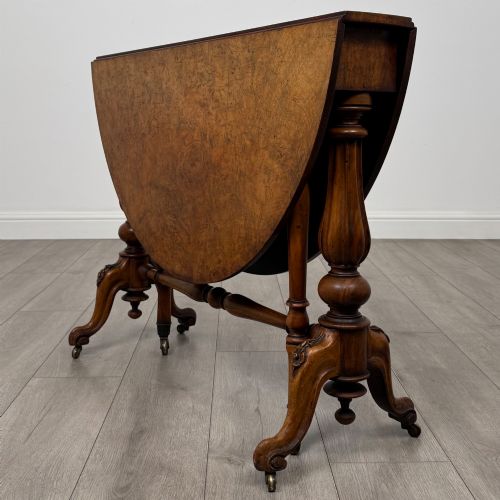 fig 7. A 19th-century Victorian Sutherland table crafted from burr walnut featuring folded drop leaves, turned twin-column supports, and carved legs on brass castors.