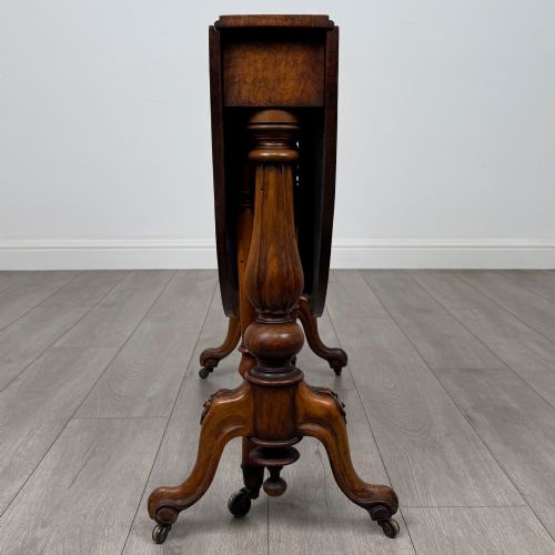 fig 8. A 19th-century Victorian Sutherland table crafted from burr walnut featuring folded drop leaves, turned twin-column supports, and carved legs on brass castors.