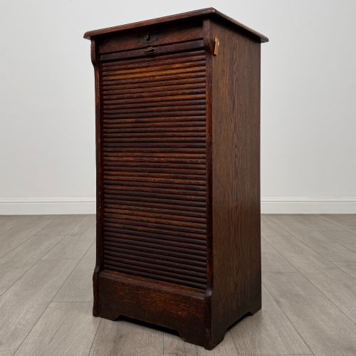 fig 2. An antique dark oak tambour cabinet featuring a vertical wooden slat roll-front door and top brass locking mechanism.