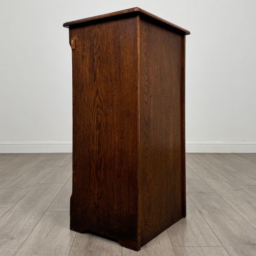 fig 4. An antique dark oak tambour cabinet featuring a vertical wooden slat roll-front door and top brass locking mechanism.