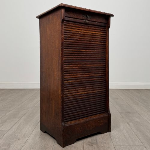 fig 8. An antique dark oak tambour cabinet featuring a vertical wooden slat roll-front door and top brass locking mechanism.