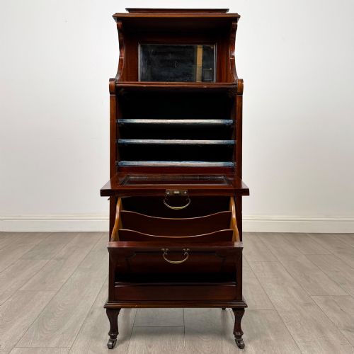 fig 1. An early 20th-century mahogany music cabinet with an upper mirrored shelf, a middle glazed drawer compartment, a lower moulded panel door, and brass handles on castors.