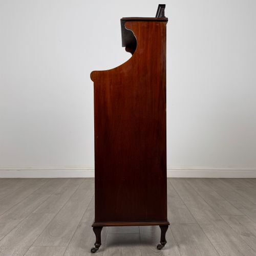 fig 3. An early 20th-century mahogany music cabinet with an upper mirrored shelf, a middle glazed drawer compartment, a lower moulded panel door, and brass handles on castors.