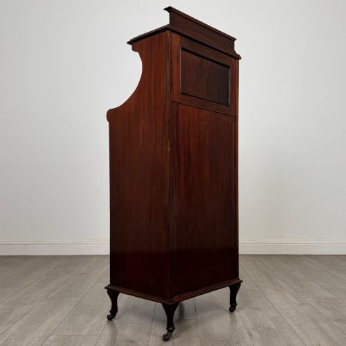 fig 4. An early 20th-century mahogany music cabinet with an upper mirrored shelf, a middle glazed drawer compartment, a lower moulded panel door, and brass handles on castors.