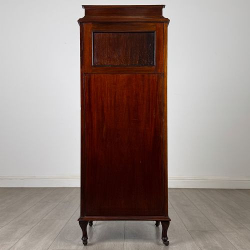 fig 5. An early 20th-century mahogany music cabinet with an upper mirrored shelf, a middle glazed drawer compartment, a lower moulded panel door, and brass handles on castors.