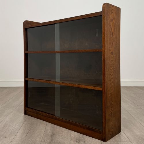 fig 2. A mid-twentieth-century dark oak display cabinet featuring three interior shelf tiers enclosed by sliding glass doors.