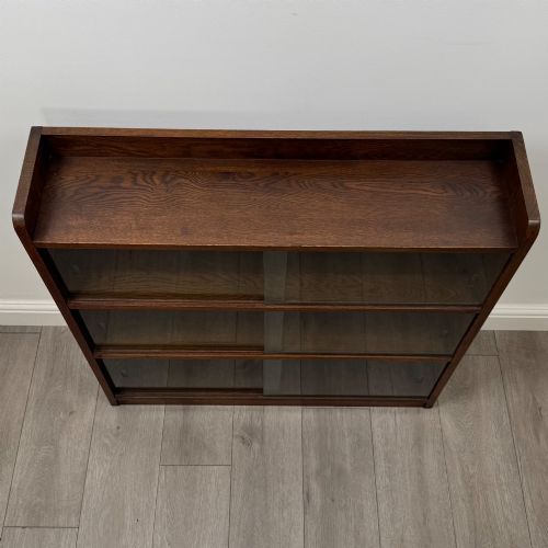 fig 9. A mid-twentieth-century dark oak display cabinet featuring three interior shelf tiers enclosed by sliding glass doors.