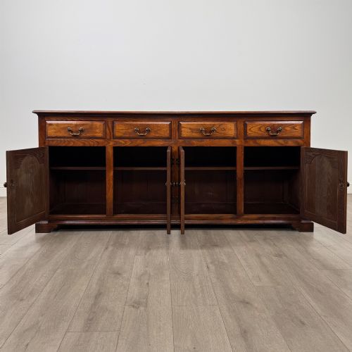 fig 1. A large medium brown oak sideboard featuring four upper drawers with brass handles above four cupboard doors with arched wood panels.