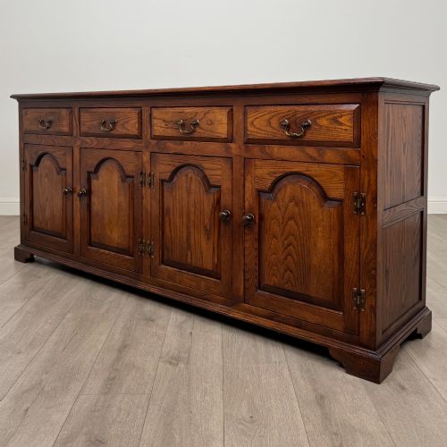 fig 2. A large medium brown oak sideboard featuring four upper drawers with brass handles above four cupboard doors with arched wood panels.