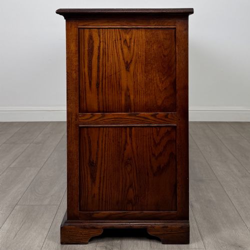fig 3. A large medium brown oak sideboard featuring four upper drawers with brass handles above four cupboard doors with arched wood panels.