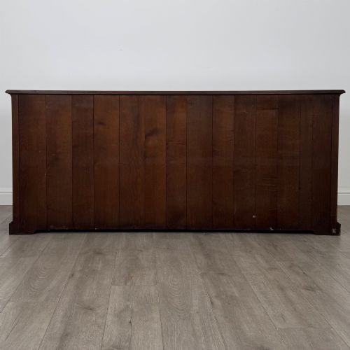 fig 5. A large medium brown oak sideboard featuring four upper drawers with brass handles above four cupboard doors with arched wood panels.