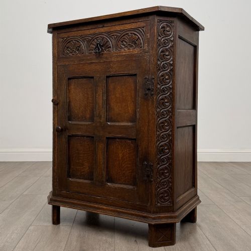 fig 2. A small dark oak cupboard featuring a single carved top drawer above a panelled cupboard door with iron hinges.