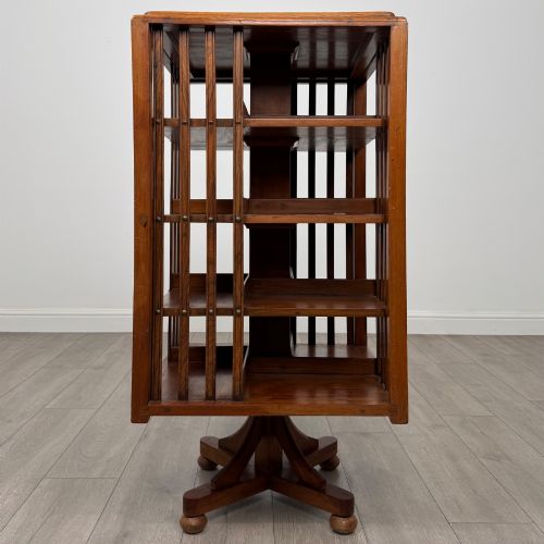 fig 2. An Edwardian oak revolving bookcase with three tier shelves, open vertical slatted sides, and a central rotating column mounted on a quadruped base with castors.
