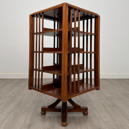 fig 3. An Edwardian oak revolving bookcase with three tier shelves, open vertical slatted sides, and a central rotating column mounted on a quadruped base with castors.