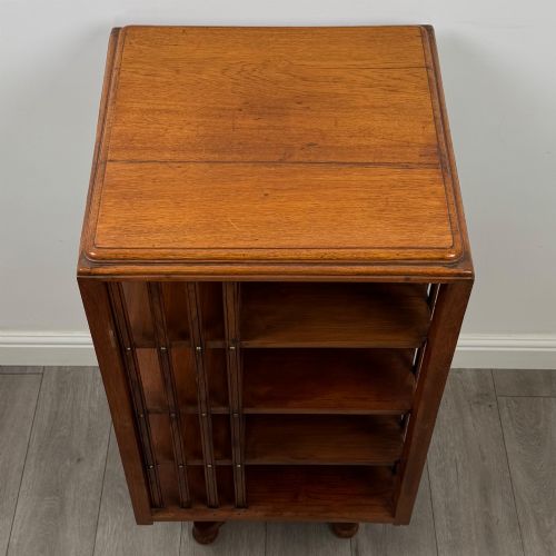fig 6. An Edwardian oak revolving bookcase with three tier shelves, open vertical slatted sides, and a central rotating column mounted on a quadruped base with castors.