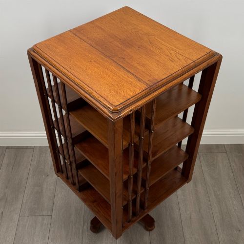 fig 7. An Edwardian oak revolving bookcase with three tier shelves, open vertical slatted sides, and a central rotating column mounted on a quadruped base with castors.
