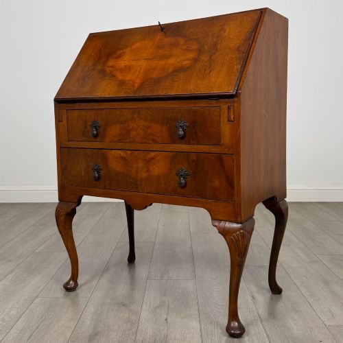 fig 2. An antique Edwardian burr walnut slant-front bureau featuring two drawers with metal handles, supported by carved cabriole legs.