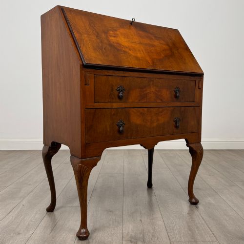 fig 8. An antique Edwardian burr walnut slant-front bureau featuring two drawers with metal handles, supported by carved cabriole legs.