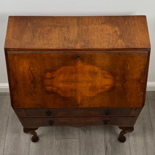fig 9. An antique Edwardian burr walnut slant-front bureau featuring two drawers with metal handles, supported by carved cabriole legs.