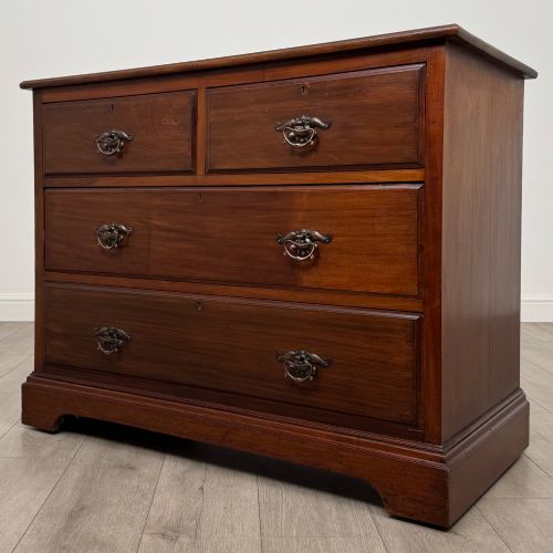 fig 1. An antique mahogany chest of drawers featuring two short top drawers over two long lower drawers with decorative metal handles on a plinth base.