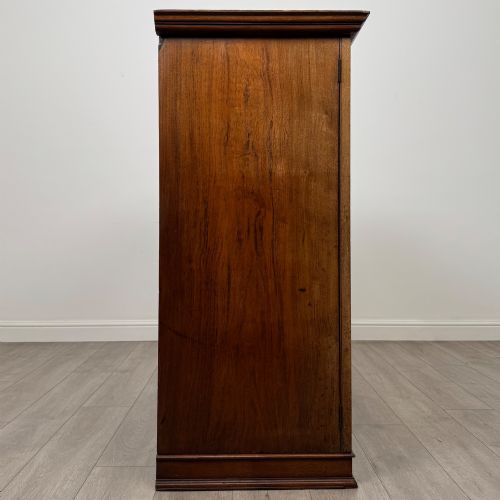 fig 7. An antique early twentieth-century two-door walnut linen cupboard featuring double panelled doors, a moulded top cornice, and a central brass teardrop handle.