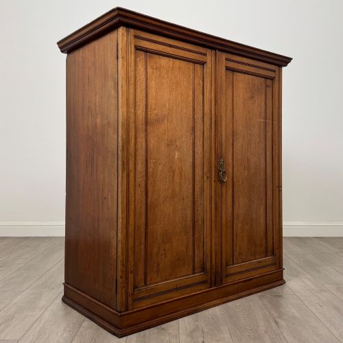 fig 8. An antique early twentieth-century two-door walnut linen cupboard featuring double panelled doors, a moulded top cornice, and a central brass teardrop handle.