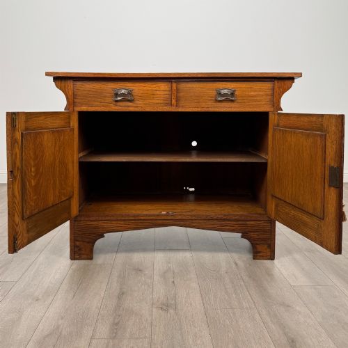 fig 1. An Arts and Crafts golden oak sideboard featuring two top drawers, two lower cupboard doors, and stylized copper strap hinges.