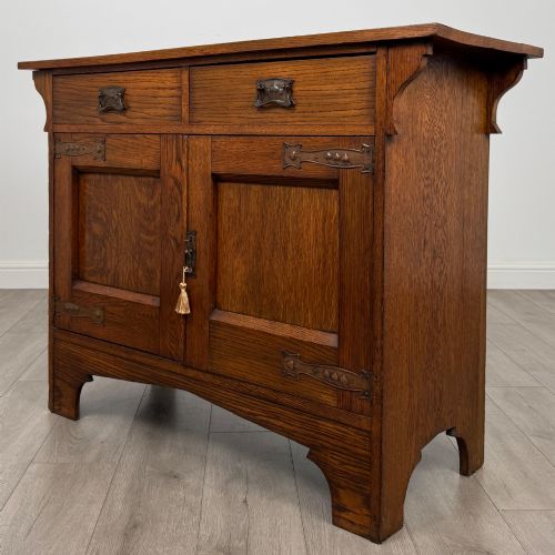 fig 2. An Arts and Crafts golden oak sideboard featuring two top drawers, two lower cupboard doors, and stylized copper strap hinges.