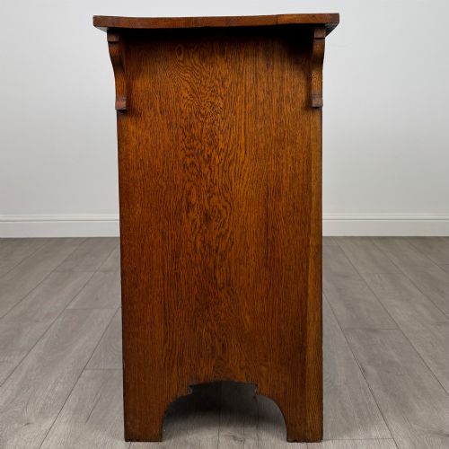 fig 3. An Arts and Crafts golden oak sideboard featuring two top drawers, two lower cupboard doors, and stylized copper strap hinges.