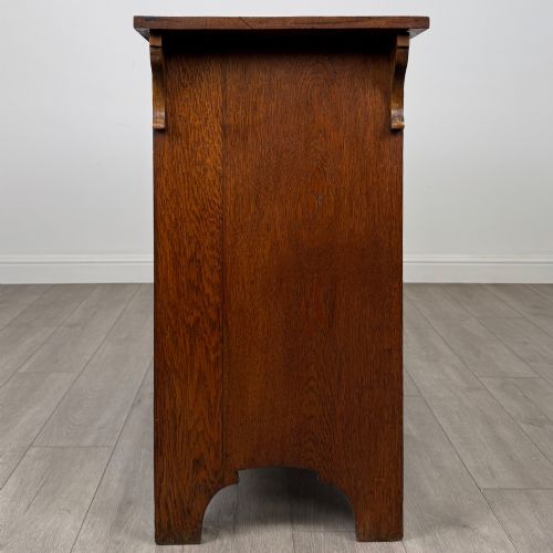 fig 7. An Arts and Crafts golden oak sideboard featuring two top drawers, two lower cupboard doors, and stylized copper strap hinges.